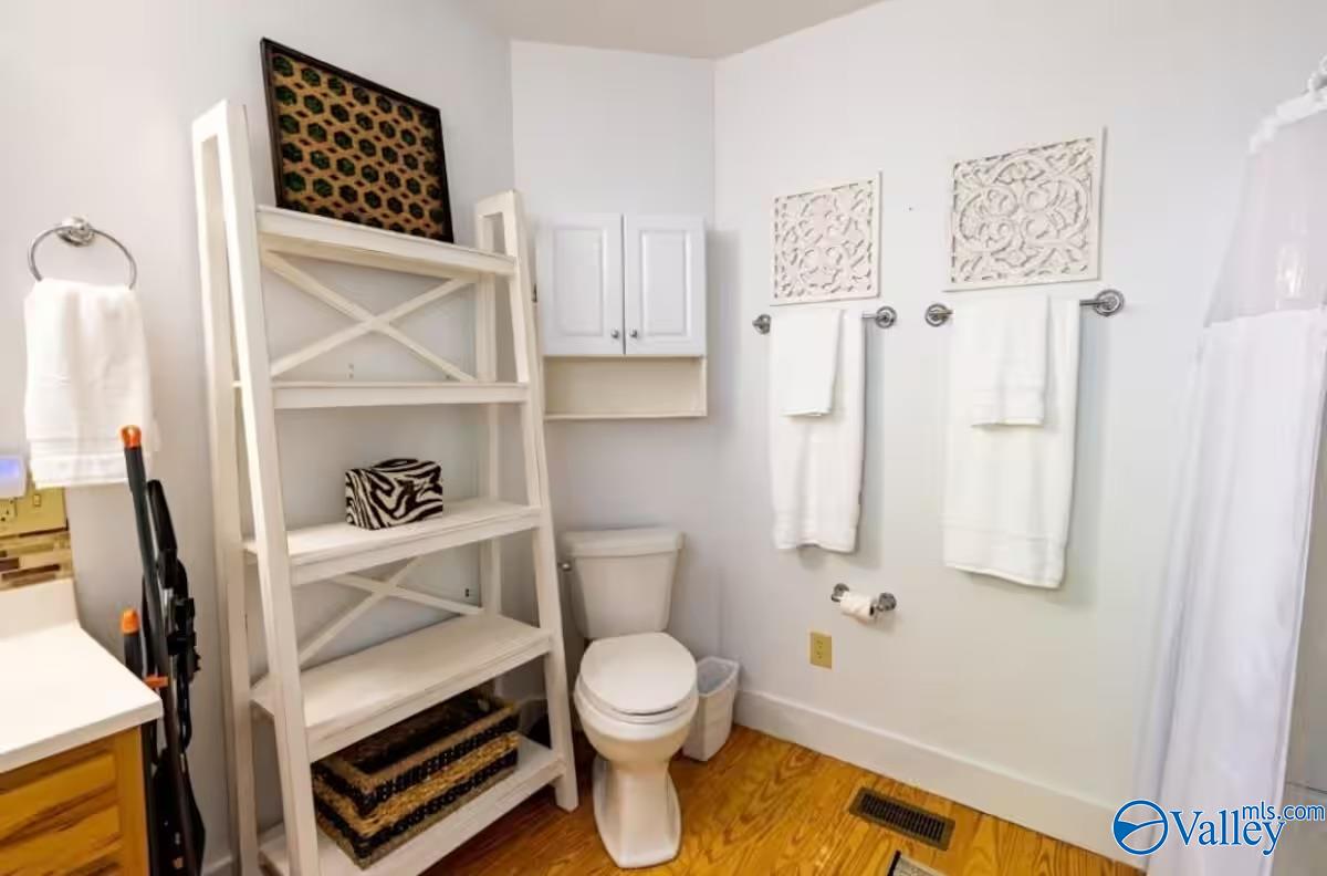 Bathroom with ladder shelving, white towels, and a toilet on a warm wood floor.