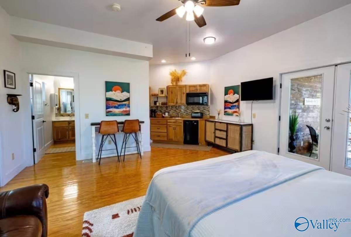 Bedroom with a foreground bed, compact wood-cabinet kitchenette, and hardwood floors.