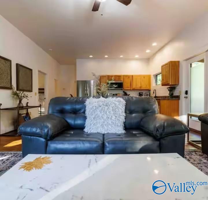 Living room with a dark blue leather sofa and white pillow facing an open kitchen with wood cabinets.