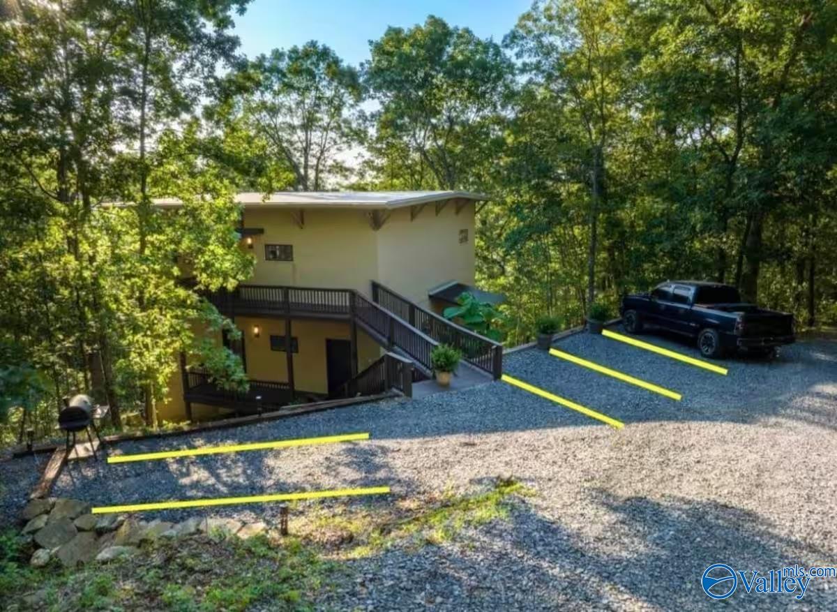 Two-story house among trees, with exterior stairs, a gravel parking area, and a pickup truck.