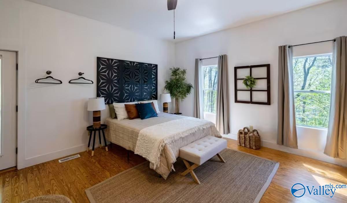 Staged bedroom with a bed beneath geometric wall panels and tall windows overlooking trees.