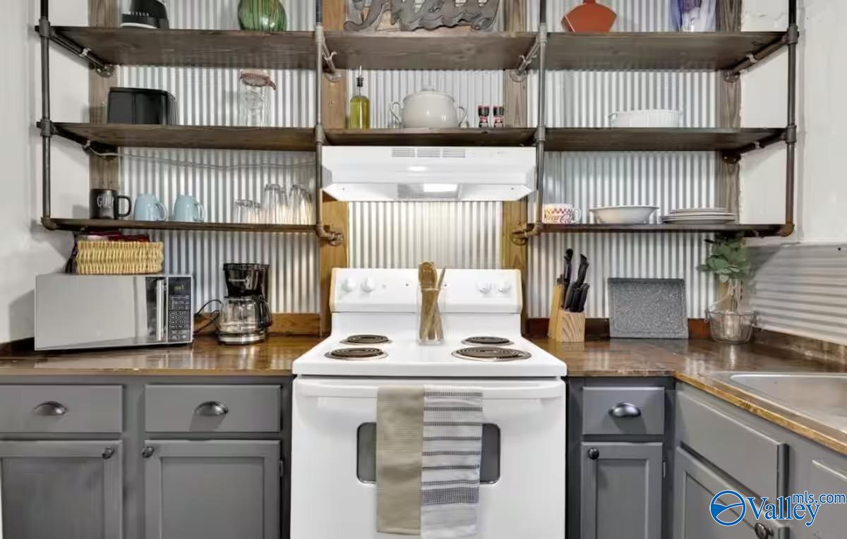 Kitchen with a white electric range, gray cabinets, butcher-block counters, and open shelves against a metal backsplash.