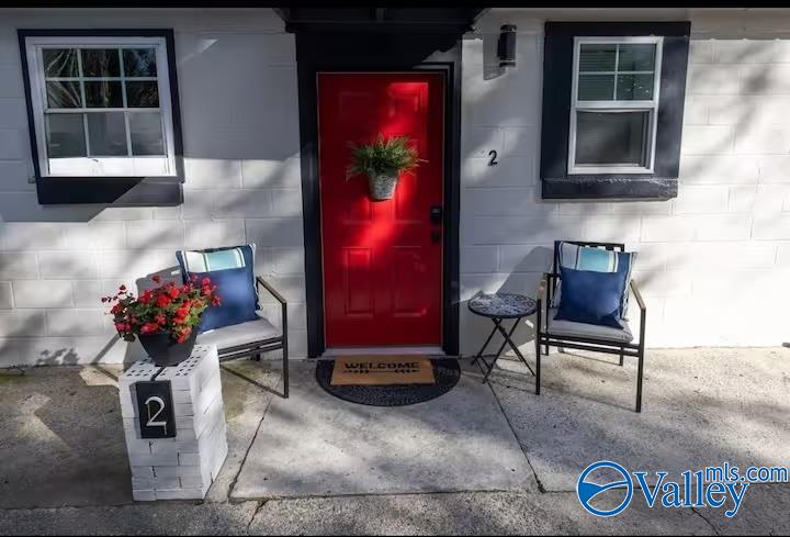 Home entrance with a bright red door, matching chairs, and flower planters.