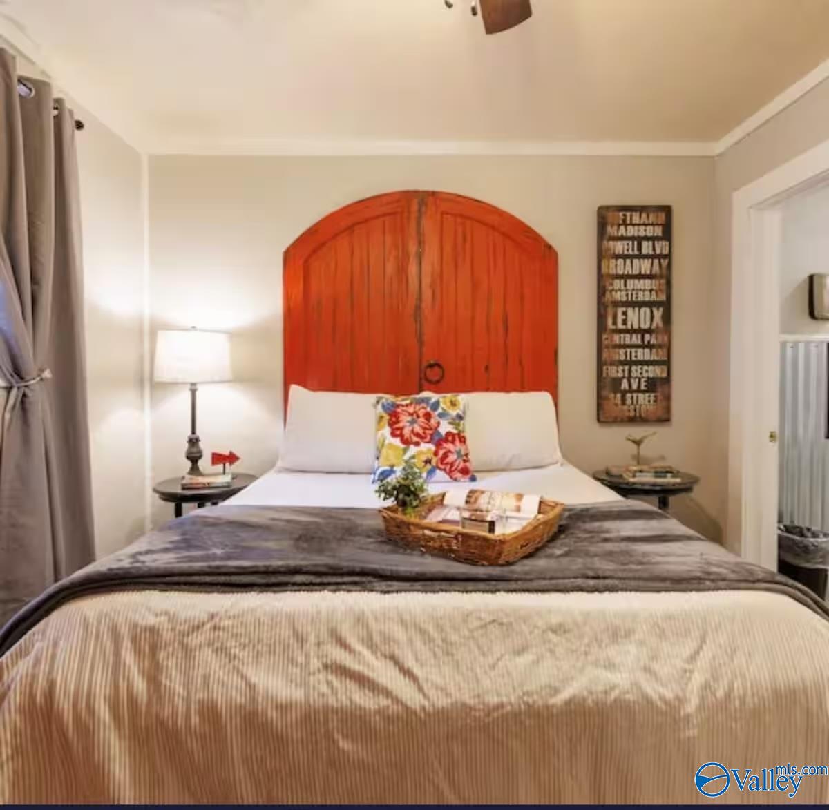 Staged bedroom with an arched red wood headboard and colorful floral accent pillow.