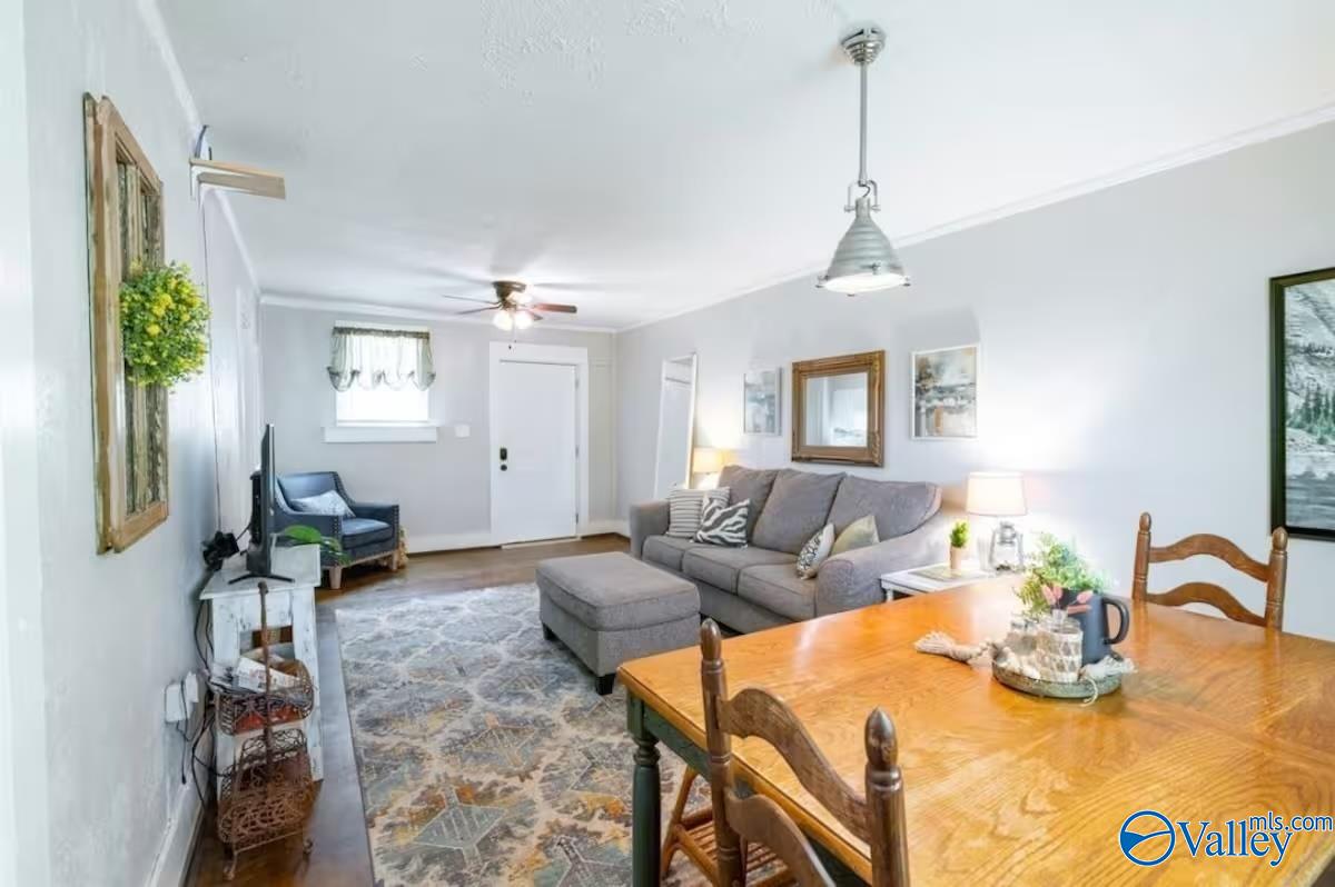 Living and dining area with a gray sofa, patterned rug, and wood dining table.