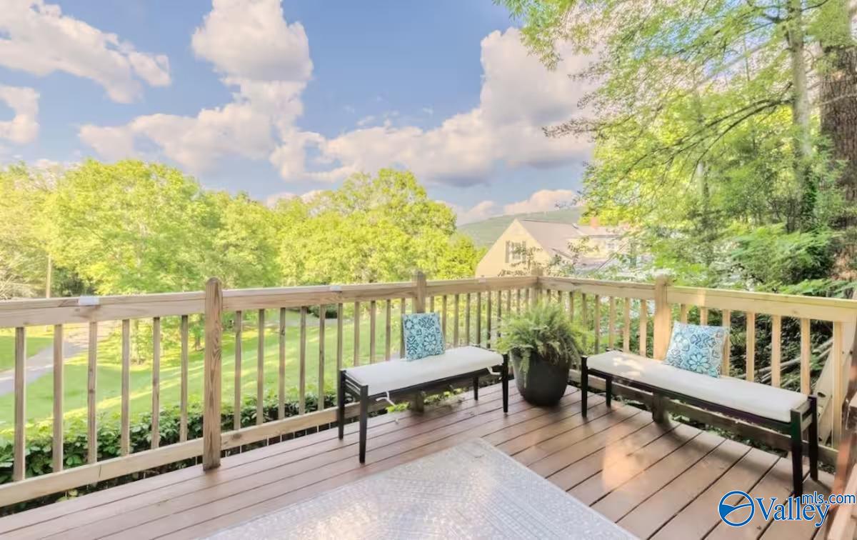 Wooden deck with cushioned benches and a potted fern overlooking a green lawn and trees.