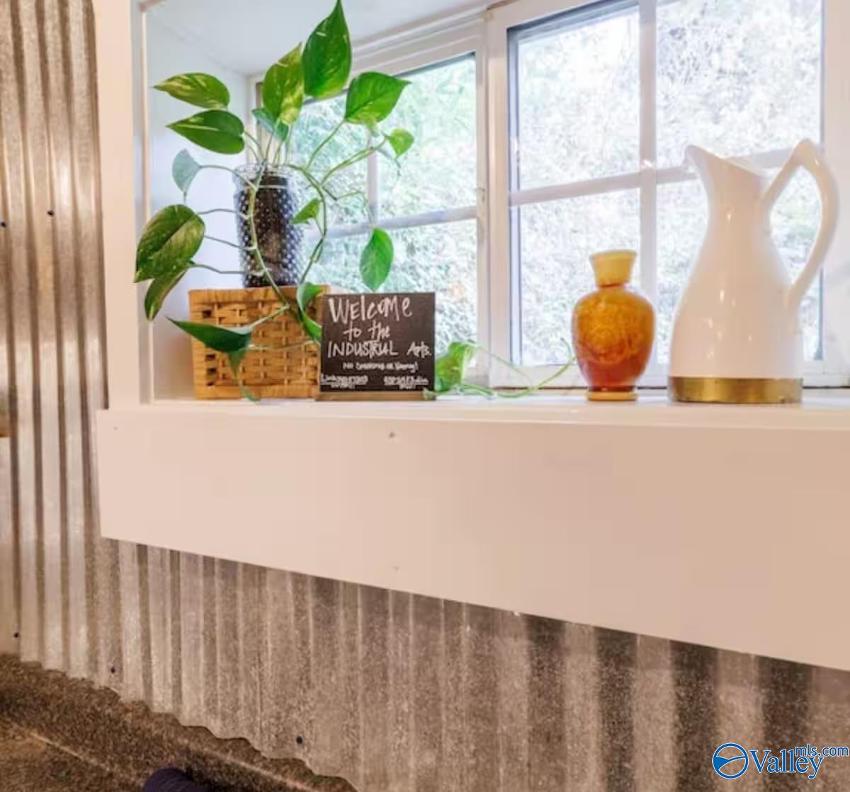 Decorated window ledge with a leafy plant, amber vase, and white pitcher above corrugated metal paneling.