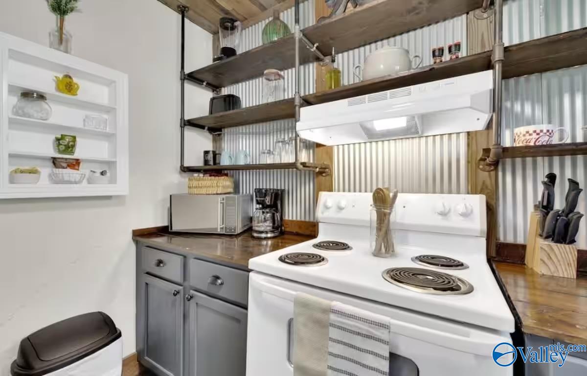 Kitchen with corrugated metal backsplash, open wood shelves, and a white electric stove.