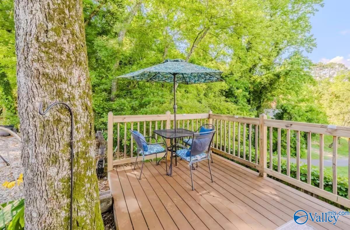 Wooden deck with patio table and chairs under an umbrella, surrounded by leafy trees.