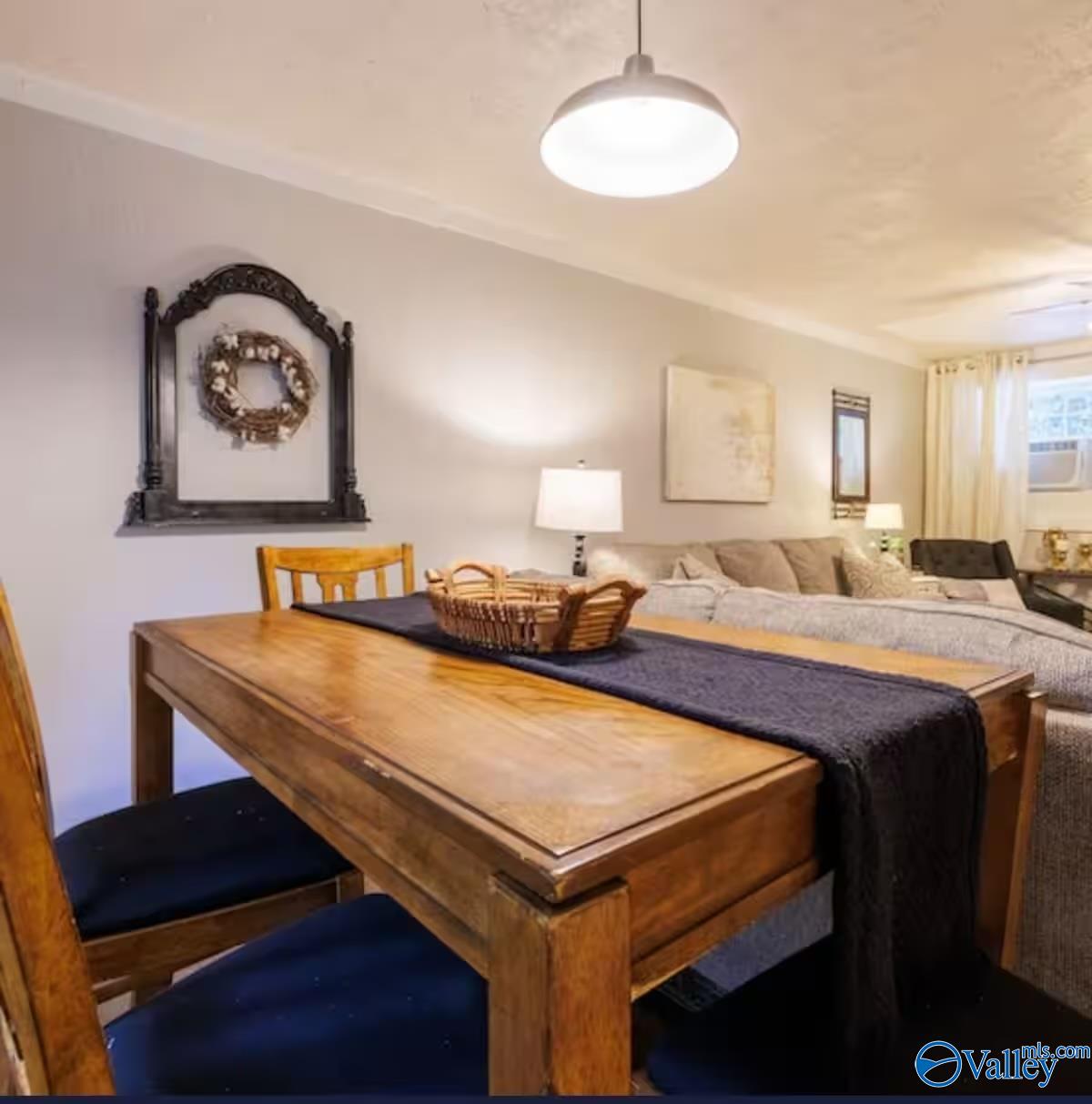 Furnished dining and living area with a wooden table, dark runner, basket, and sofa.