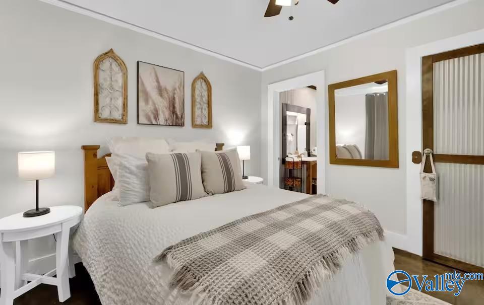 Furnished bedroom with a large white bed, gray throw, matching bedside lamps, and decorative wall art.