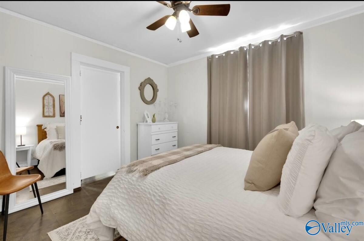 Bedroom with a white bed, beige curtains, ceiling fan, and full-length mirror.