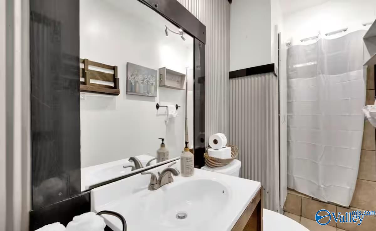Bathroom with a white vanity, large dark-framed mirror, and curtained shower.