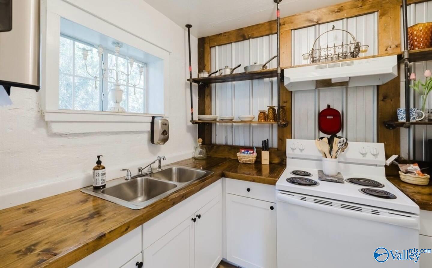 Kitchen with butcher-block counters, a double sink beneath a window, and a white electric range.