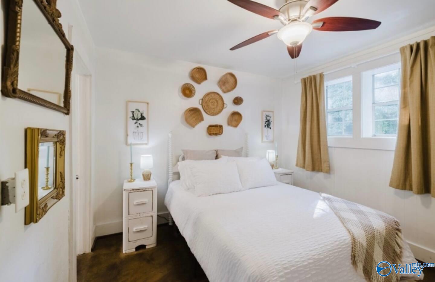 Bedroom with a white bed, woven basket wall decor, and tan-curtained windows.
