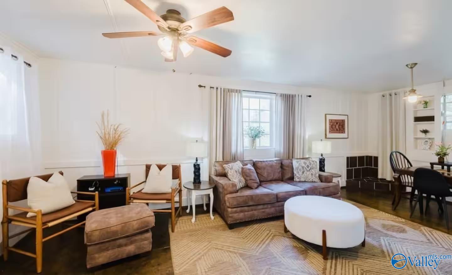 Staged living room with a brown sofa, wood-framed chairs, and a white oval coffee table.