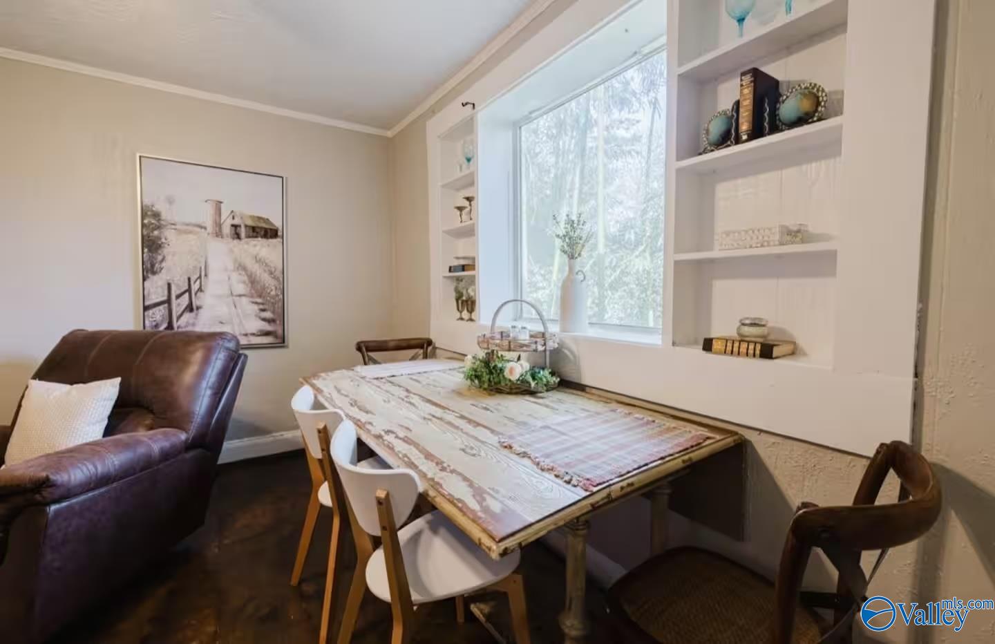 Dining area with a rustic table, built-in shelves, large window, and brown leather armchair.