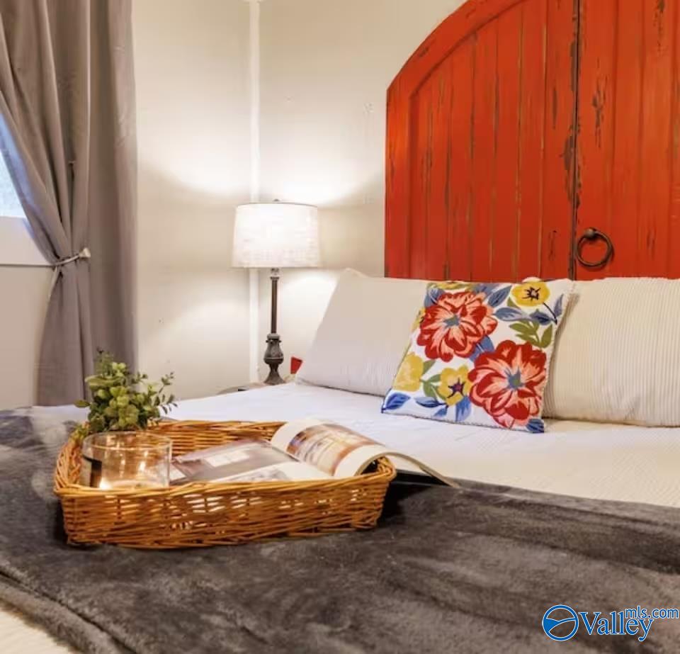 Bedroom with white bedding, vivid red paneled headboard, and floral accent pillow.