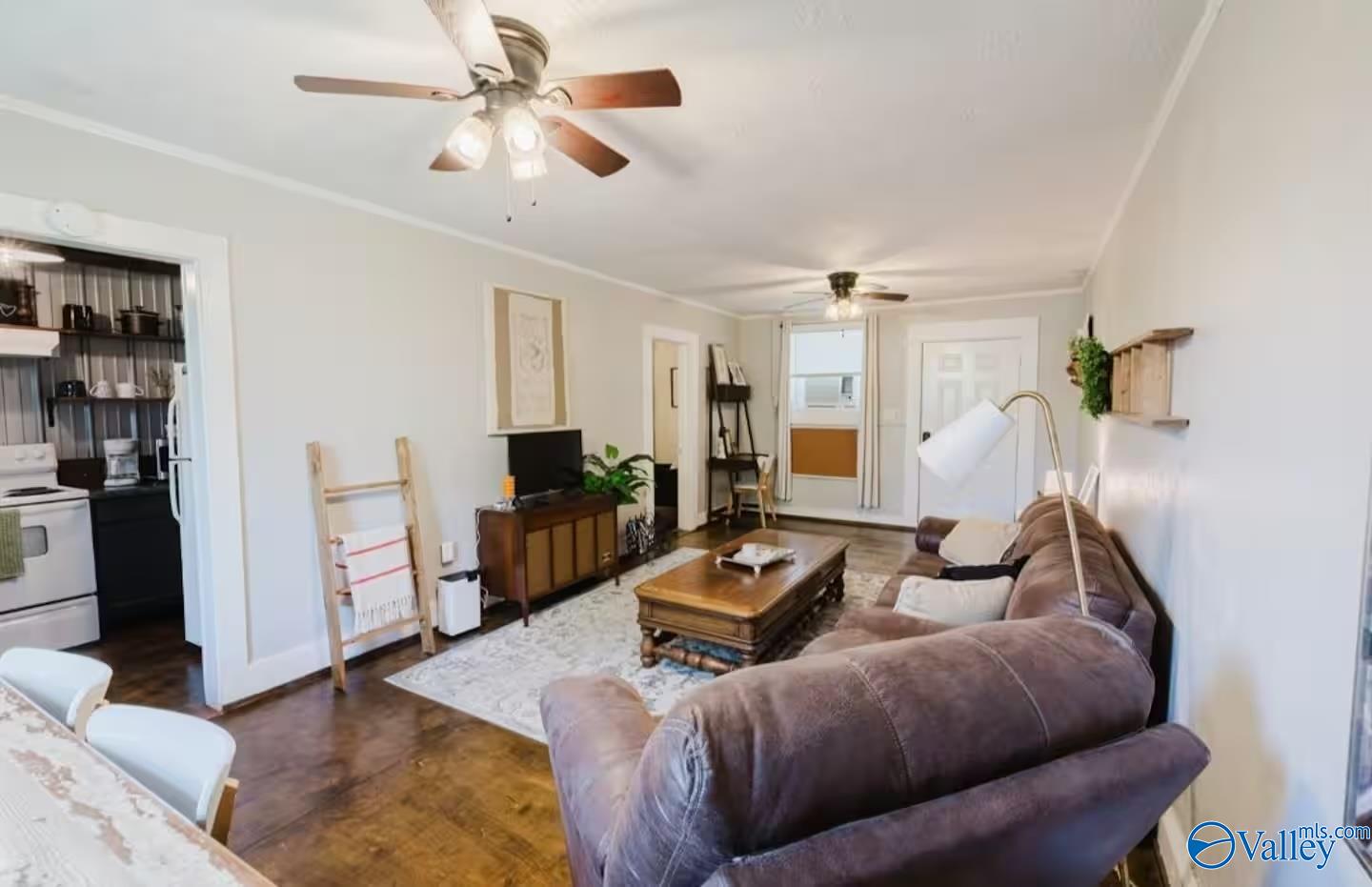 Living room with a brown sectional, carved wooden coffee table, ceiling fans, and adjoining kitchen.