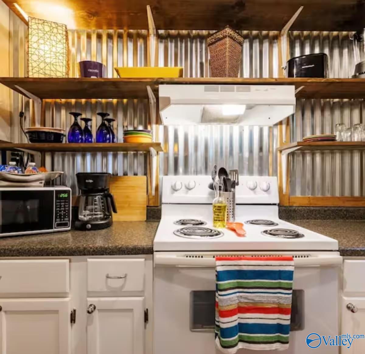 Kitchen with a white electric range, speckled countertops, and open wooden shelves against corrugated metal walls.