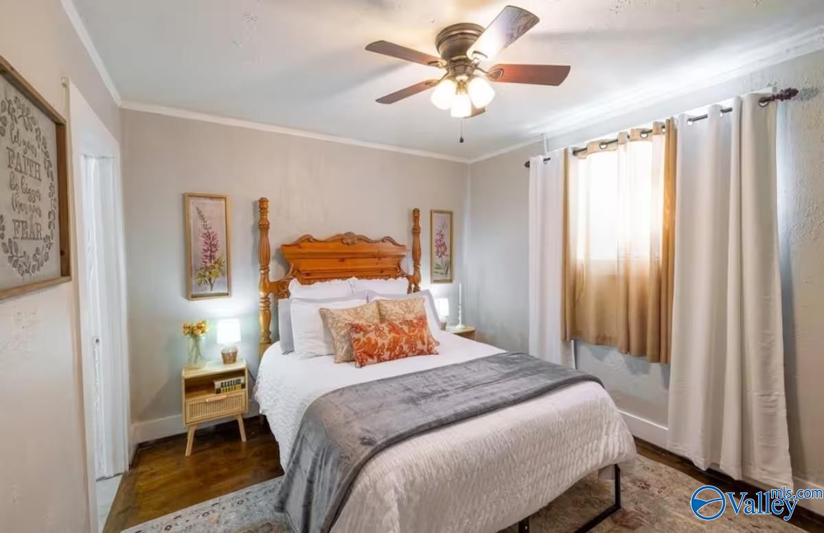 Bedroom with a carved wooden four-poster bed, gray throw, ceiling fan, and bright curtained windows.