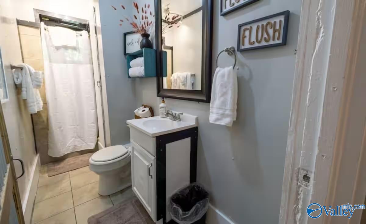 Bathroom with a white vanity, toilet, tiled floor, and curtained shower.