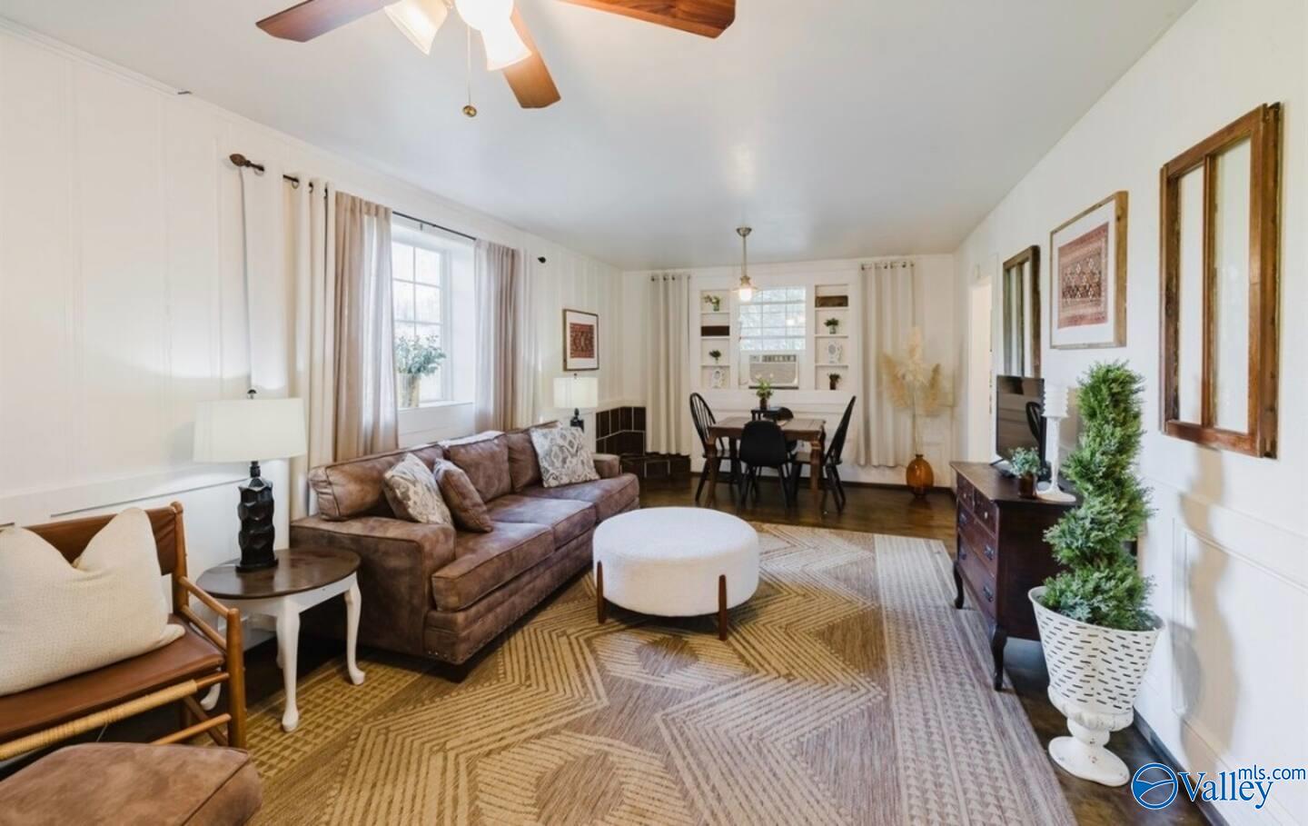 Living room with a brown sofa and patterned rug, opening into a dining area with built-in shelves.