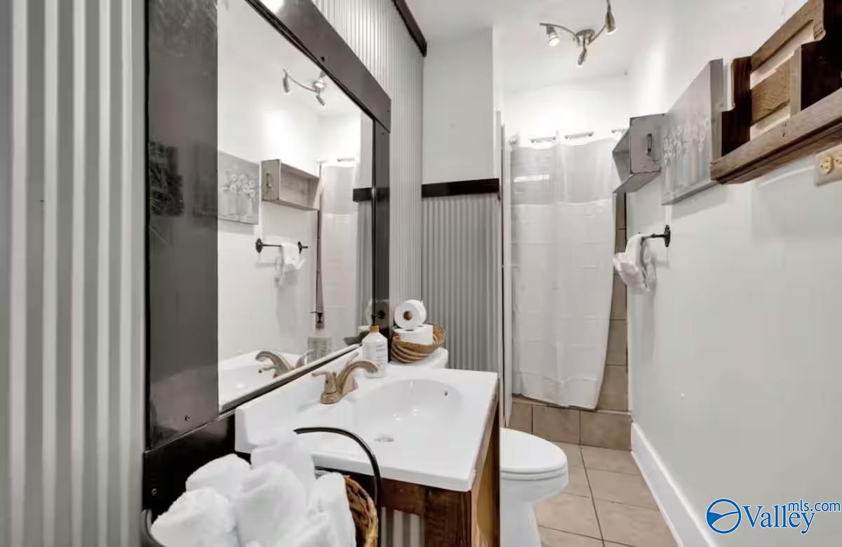 Bathroom with a large mirror, white vanity, and curtained shower beside the toilet.