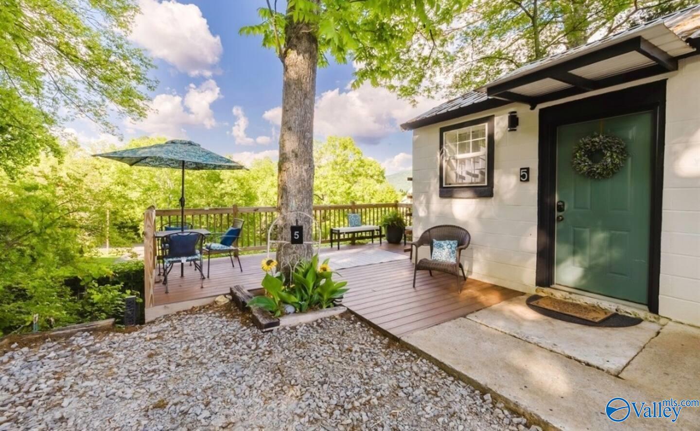 Home entrance with a green door and furnished wooden deck beneath a large shade tree.