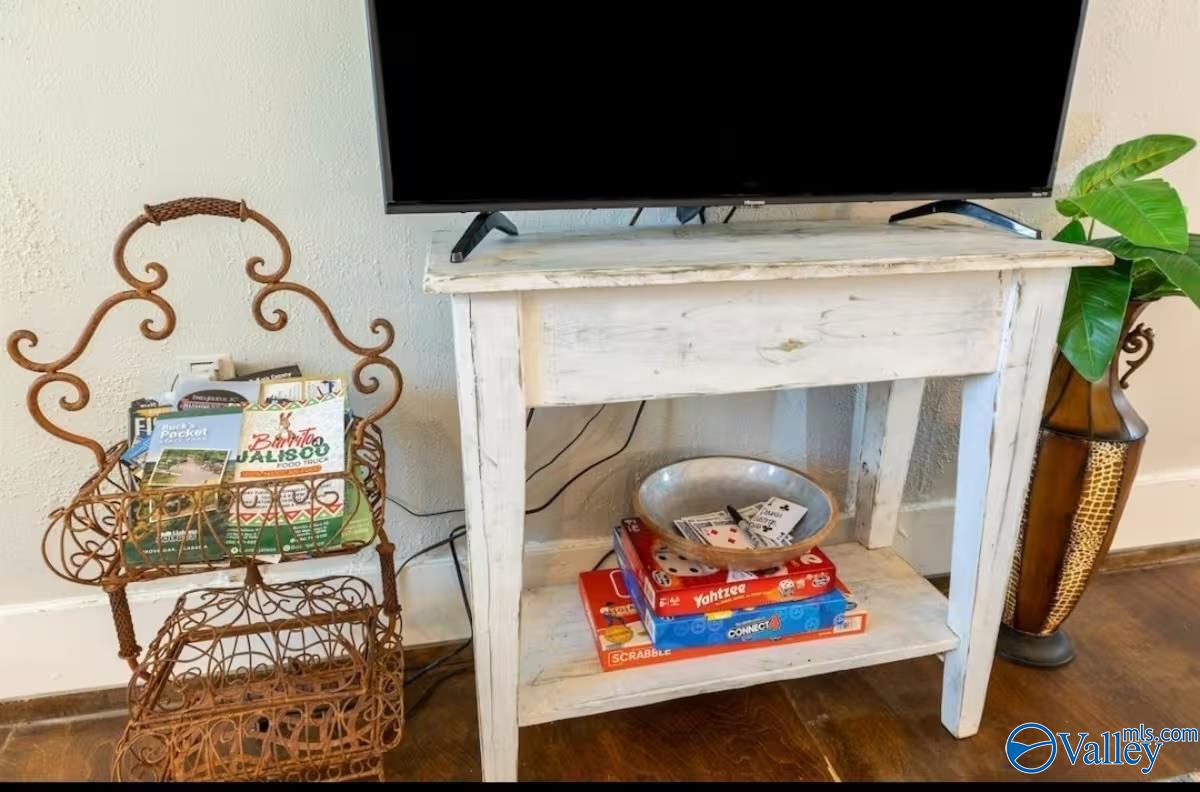 Whitewashed living room console with a television, board games, and a wrought-iron magazine rack.