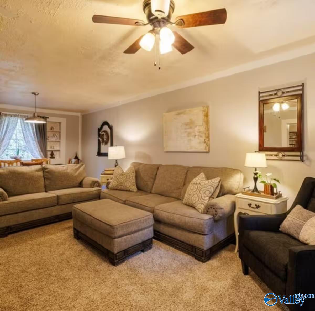 Furnished living room with beige sectional sofas, a matching ottoman, and a ceiling fan with lights.