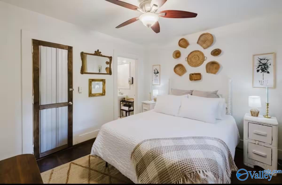 Furnished bedroom with a white bed, woven basket wall decor, and a dark wood paneled door.