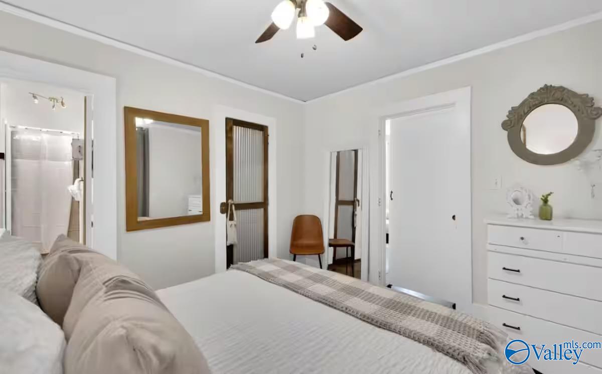 Bedroom with a large bed, ceiling fan, white dresser, and doorway to an adjoining bathroom.