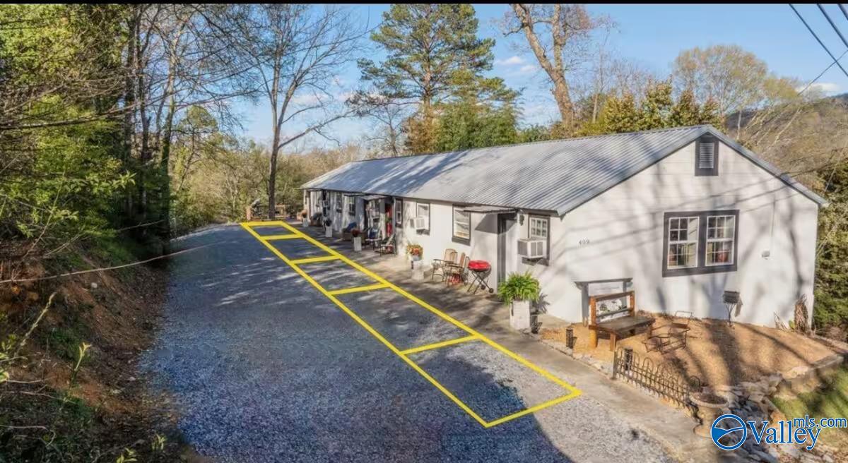 Single-story white house with a metal roof beside a gravel driveway marked for parking.