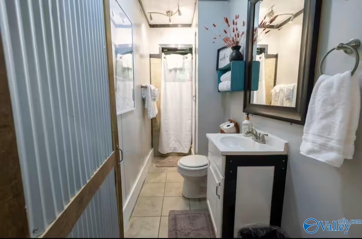 Bathroom with a white vanity, toilet, and curtained shower beside a blue corrugated partition.