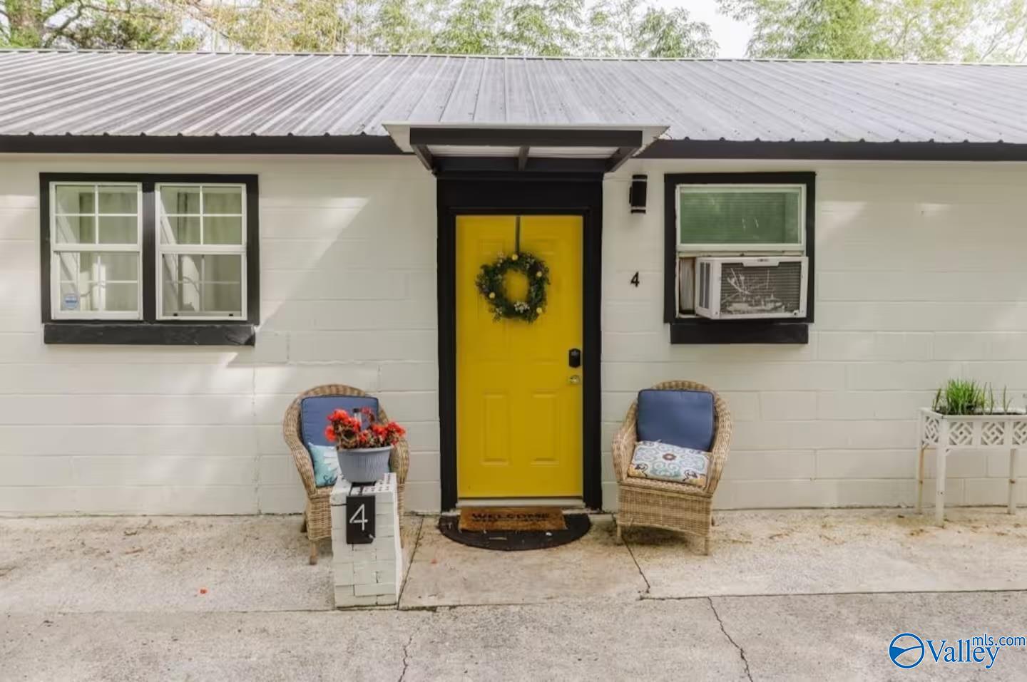 Home exterior with a bright yellow front door, gray metal roof, and wicker chairs by the entrance.