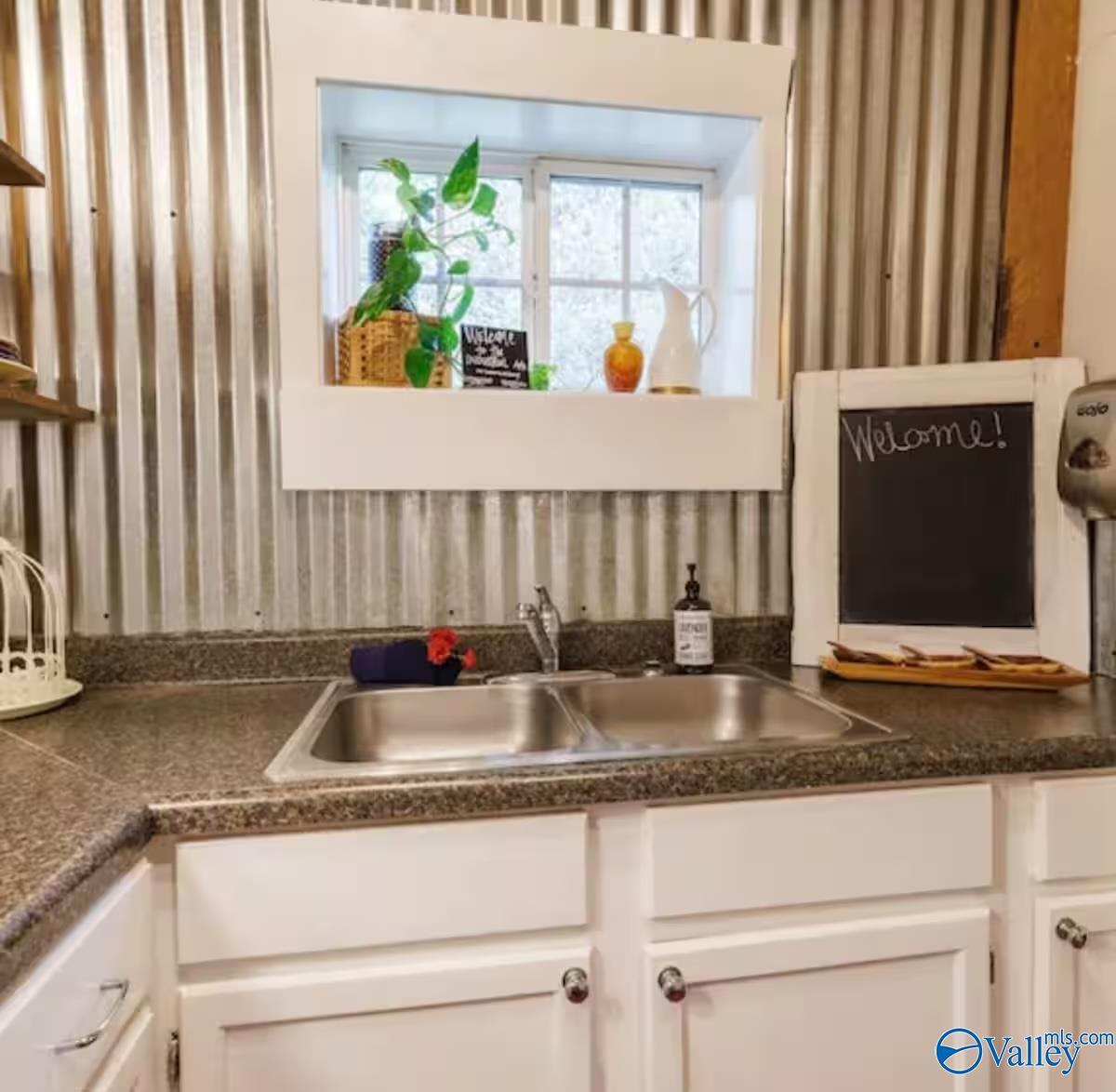 Kitchen sink beneath a small window, with a corrugated metal backsplash and a welcome chalkboard.