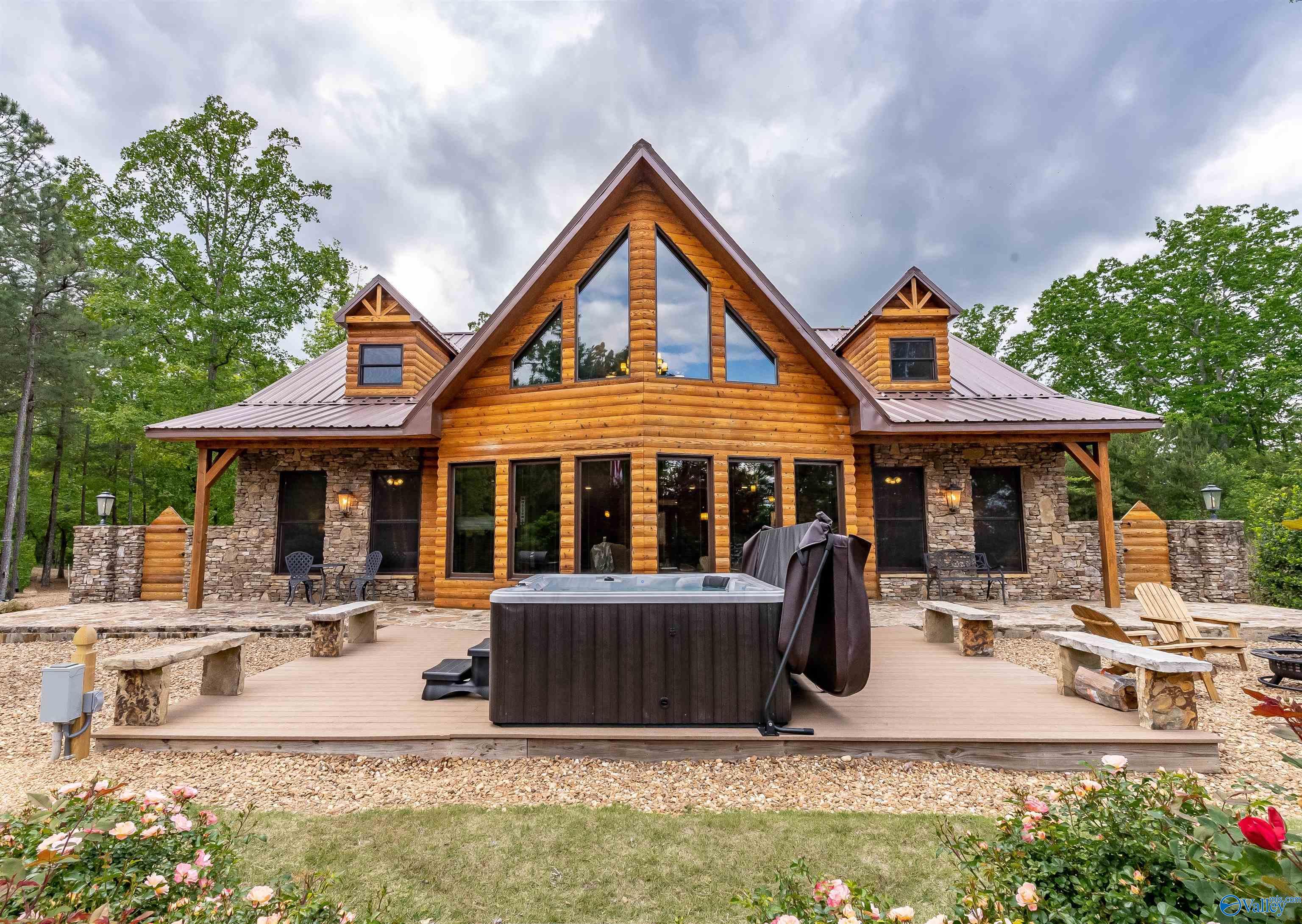 Log-and-stone home with a steep roof, hot tub, and seating on a broad wooden deck.