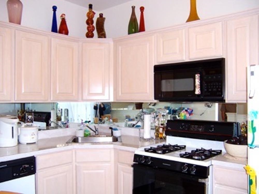 Kitchen with pale cabinets, mirrored backsplash, and a black gas range beneath a built-in microwave.