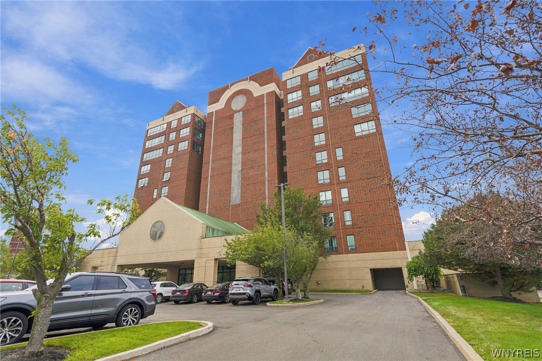 Red-brick condominium building with a beige entrance and parking area.