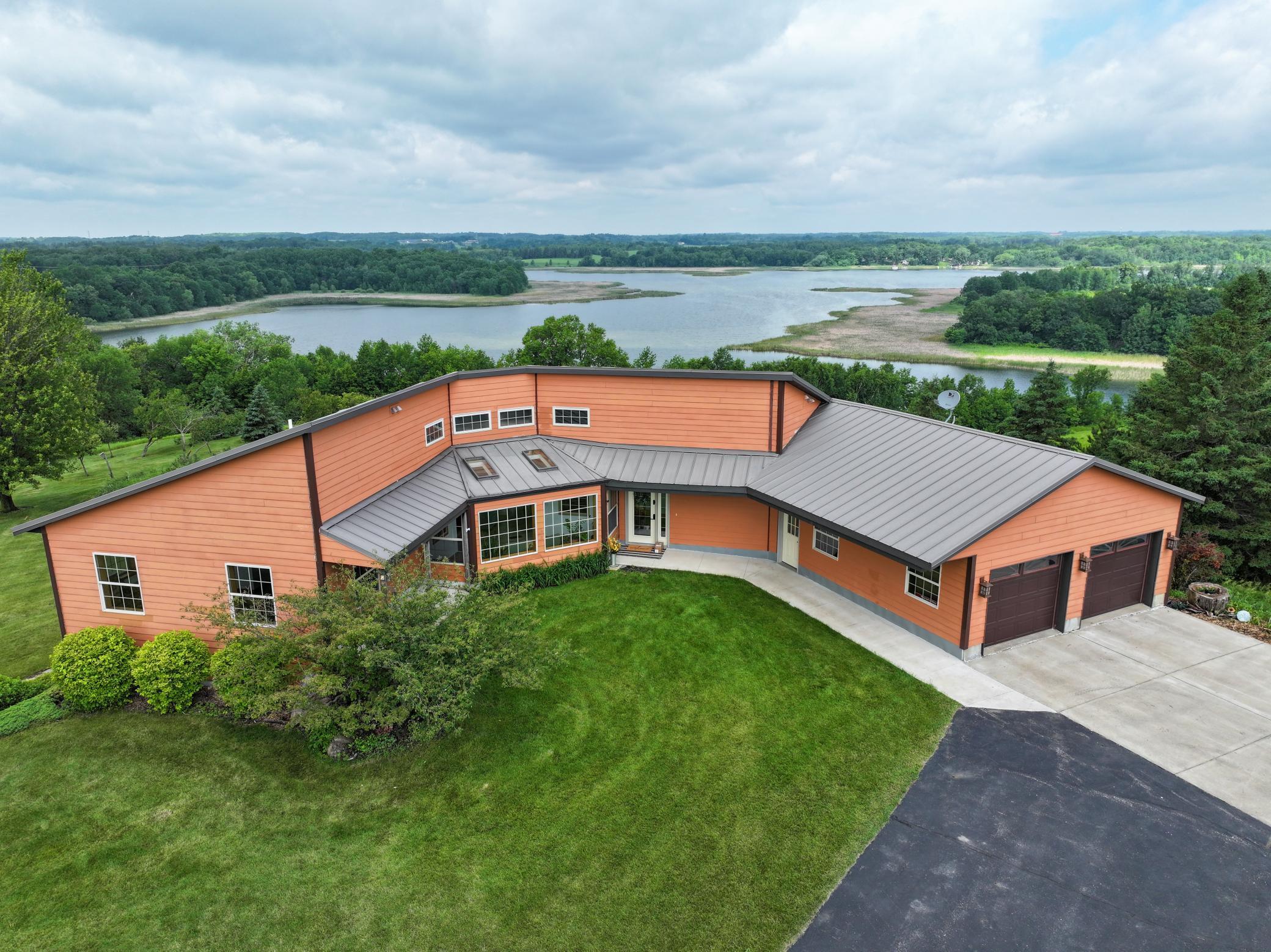 Orange-sided home with a gray metal roof overlooks a lake and wooded shoreline.