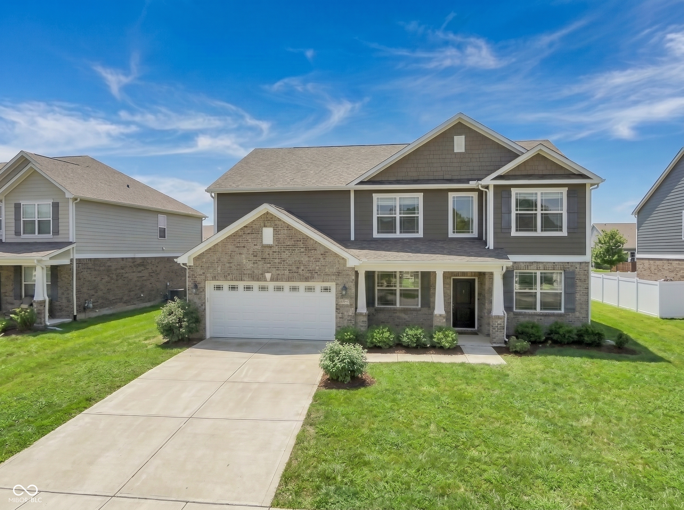 Two-story gray and brick home with an attached garage, wide driveway, and green lawn.