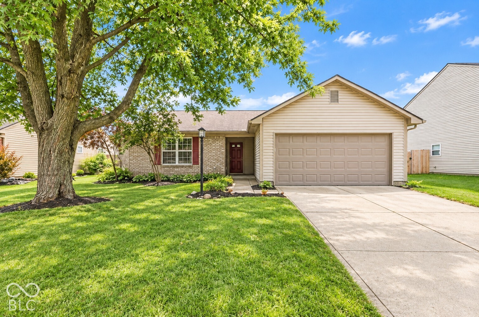 Single-story home with brick accents, a two-car garage, and a large shade tree in the front yard.