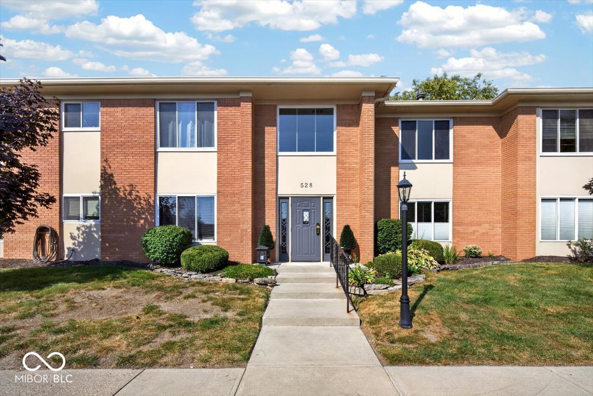 Brick residential building entrance numbered 528, with a central walkway and landscaped shrubs.