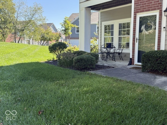 Covered patio with outdoor dining set beside a brick home, overlooking a green lawn.
