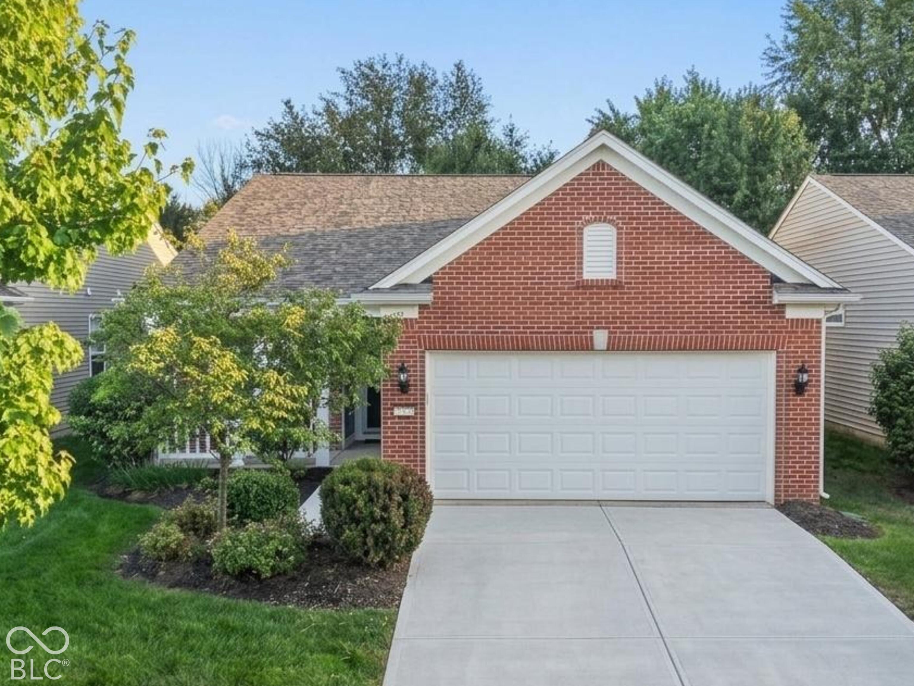 Red brick house with a white double garage, landscaped front yard, and wide concrete driveway.