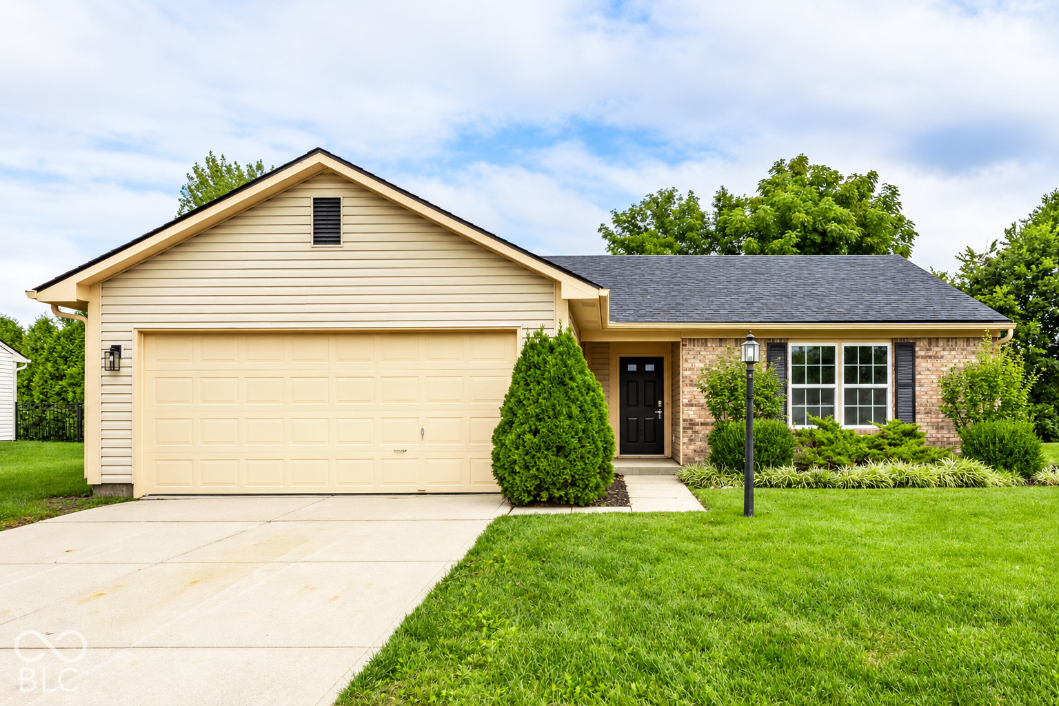 Single-story home with a beige two-car garage, brick facade, and landscaped front yard.