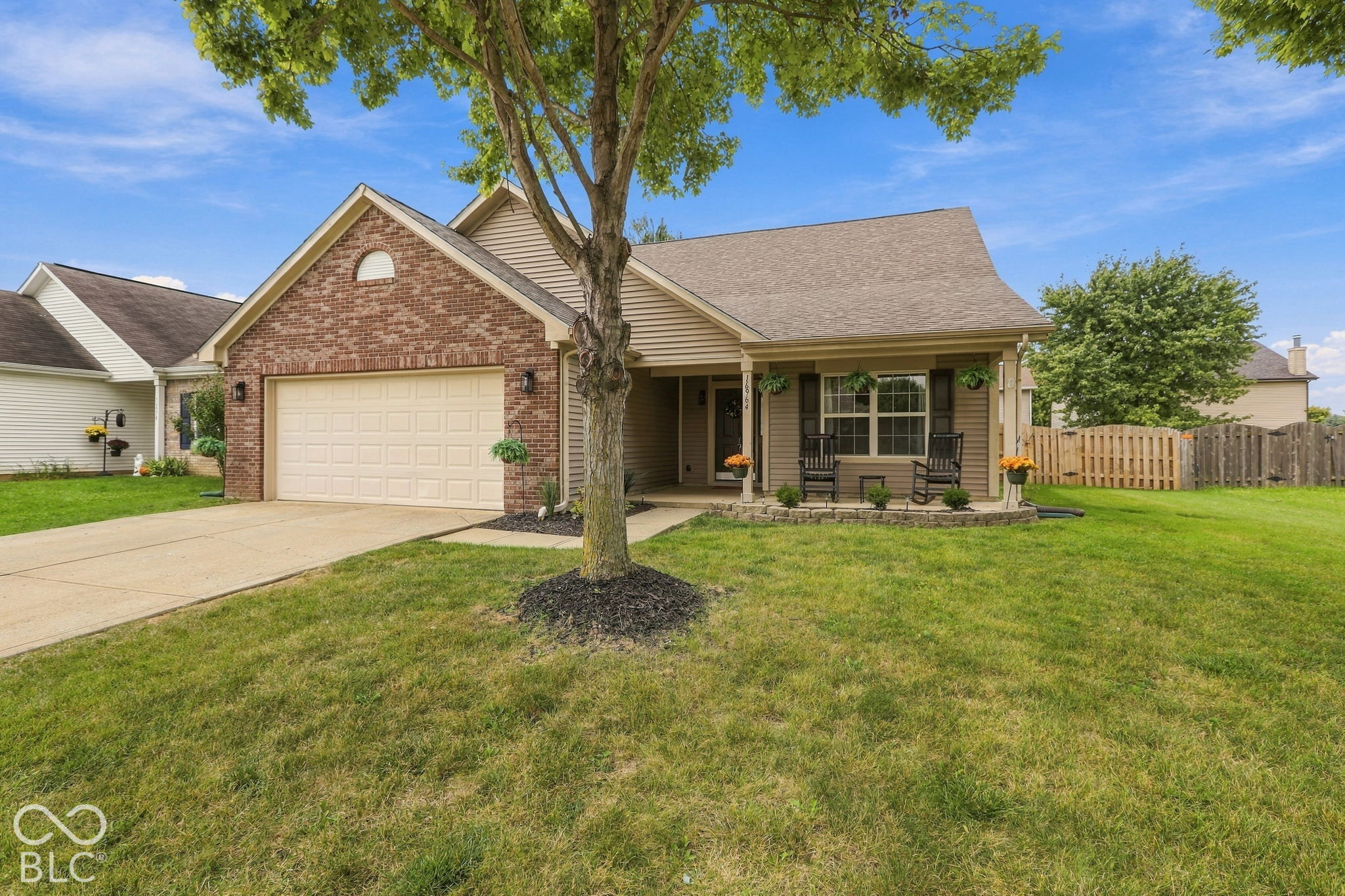 Suburban home with a brick front gable, attached garage, and covered porch with rocking chairs.