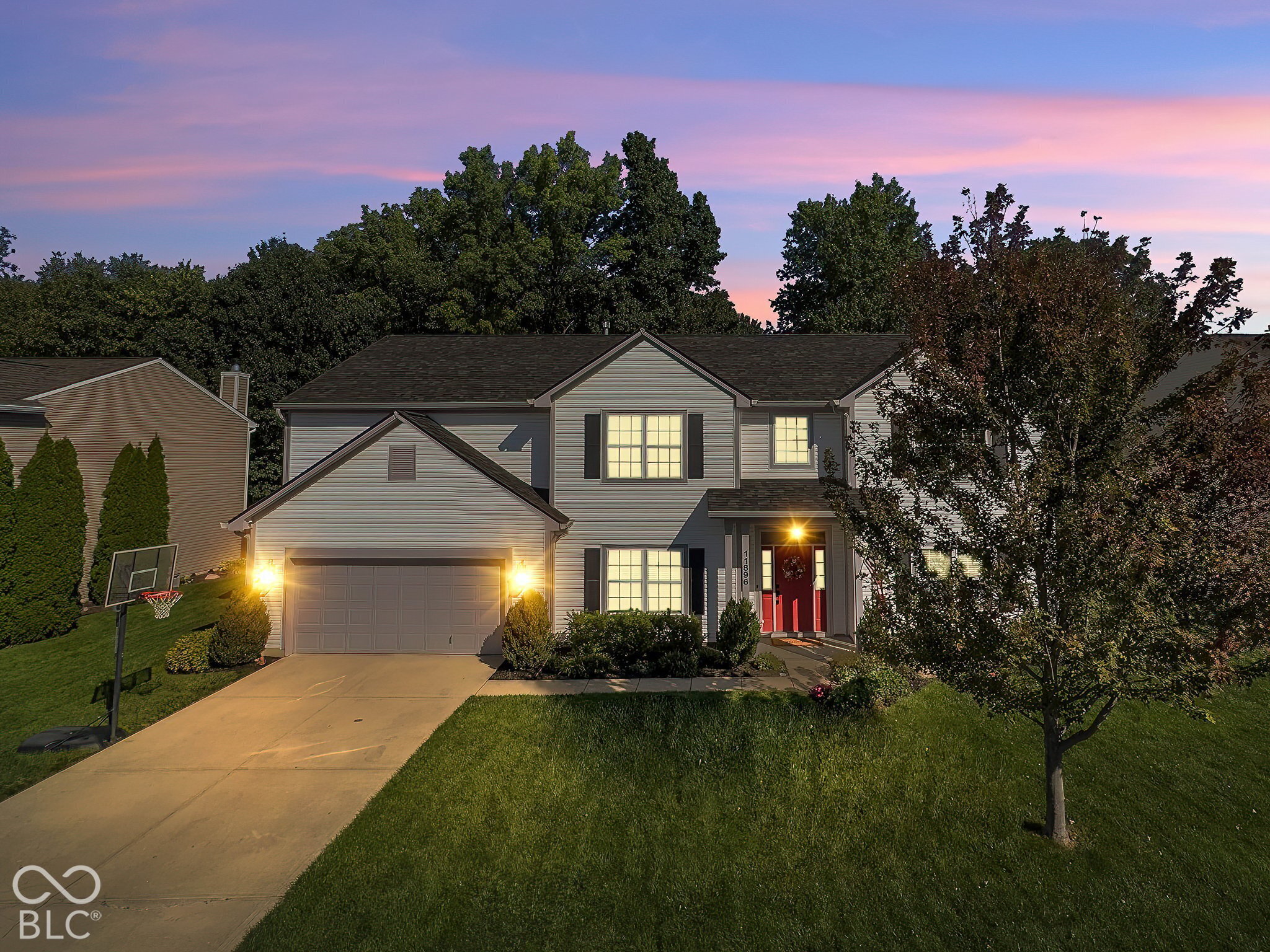 Two-story gray house with a red front door and lit windows at dusk.
