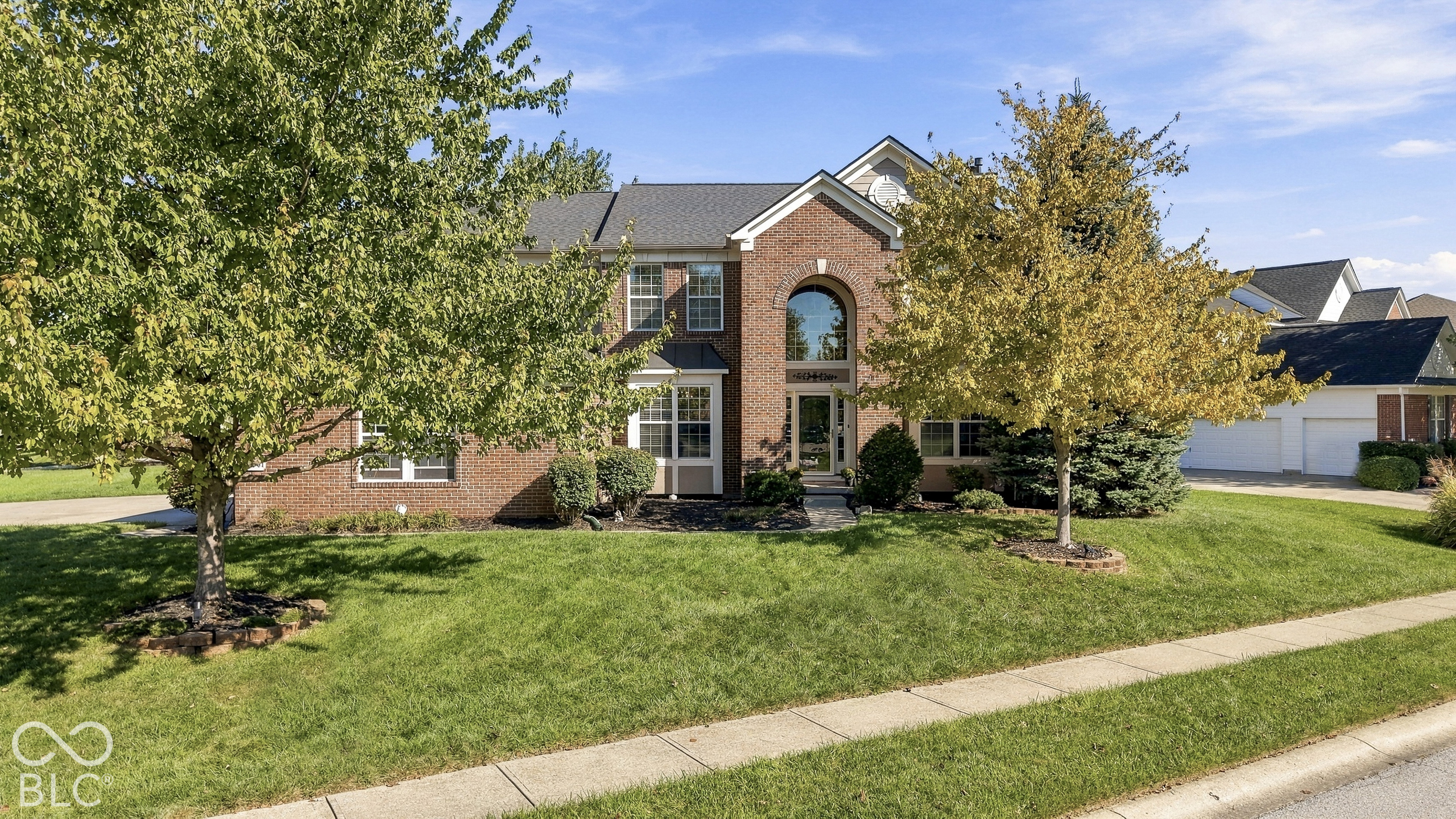 Two-story brick house with an arched entry window, mature trees, and a broad front lawn.